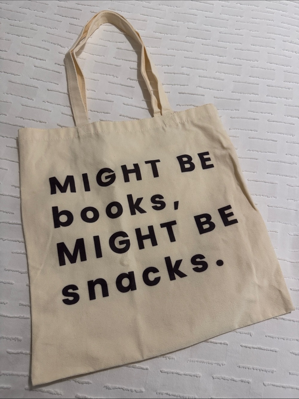 Cream Canvas Tote Bag with Black Text "MIGHT BE books, MIGHT BE snacks.",